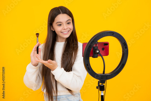 Beauty blog  presenting makeup cosmetics powder and brush. Teen girl speaking in front of camera for vlog isolated on yellow background. Teenager working as blogger  recording video blog.