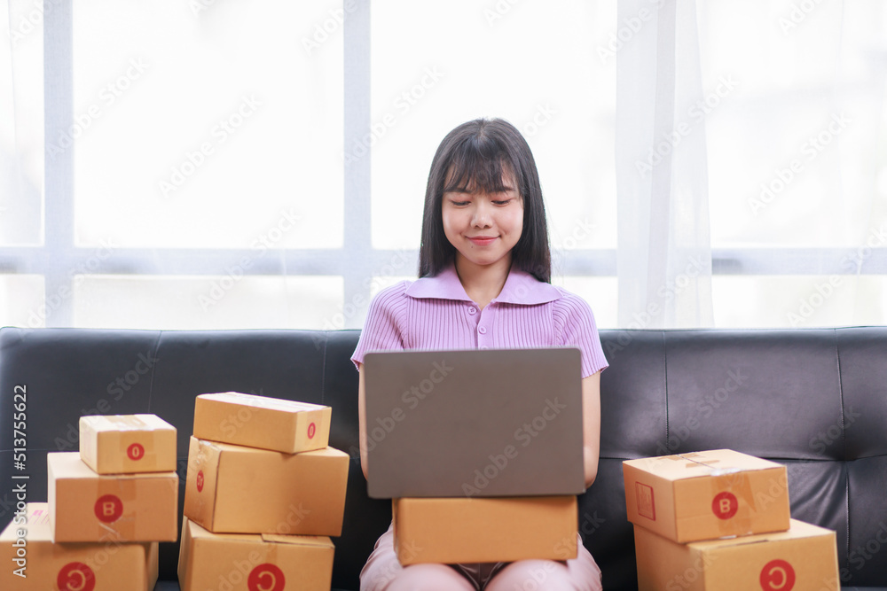 Startup SME small business entrepreneur of freelance using a laptop with box, Asian business woman on sofa check online orders to prepare to pack the boxes sell to customers sme business ideas online. Startup SME small business entrepreneur of freelance using a laptop with box, Asian business woman on sofa check online orders to prepare to pack the boxes sell to customers sme business ideas online.