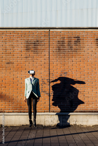 Businesswoman with VR goggles jumping in front of wall photo