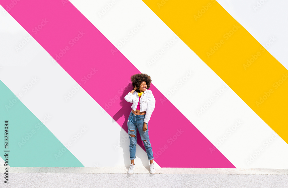 Smiling young woman standing in front of colorful wall on sunny day Smiling young woman standing in front of colorful wall on sunny day