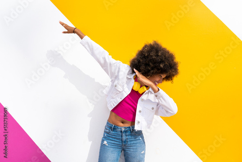 Playful young Afro woman doing dab dance in front of colorful wall photo