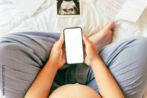 Pregnancy smartphone screen. Pregnant woman holding smartphone mock up. Mobile pregnancy online maternity application. Concept of pregnancy, maternity, expectation for baby birth.