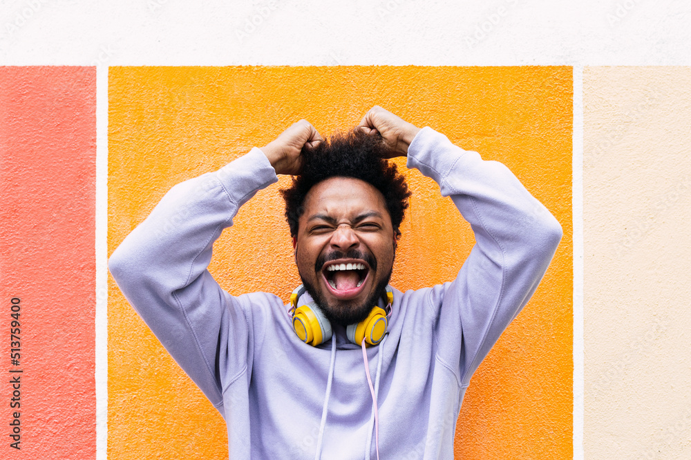 © VISTA by Westend61 - Excited man with arms raised screaming in front of orange wall