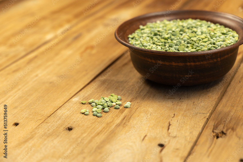 Dry split peas in a bowl against a wooden background. Green pea beans in brown earthenware bowl. Uncooked food. Healthy food. Close-up. Selective focus. Copy space for text and design elements. Dry split peas in a bowl against a wooden background. Green pea beans in brown earthenware bowl. Uncooked food. Healthy food. Close-up. Selective focus. Copy space for text and design elements.