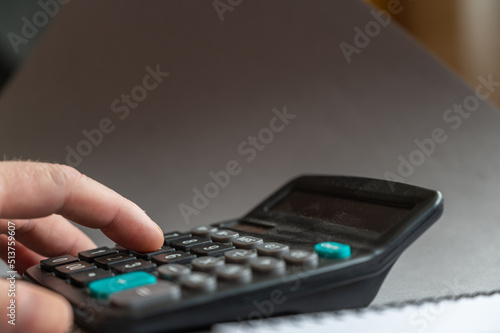 Close-up of a man's hand doing calculations on a calculator. Index finger presses button on the dusty device. Side view. Selective focus.