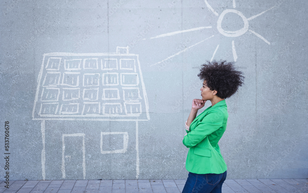 Young woman looking at painted house with solar panels on wall Young woman looking at painted house with solar panels on wall