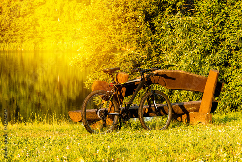 Sport bicycle leaning against wooden bench at lakeside photo