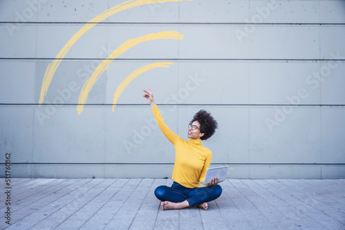 Woman sitting on ground holding laptop connected through WiFi sign photo