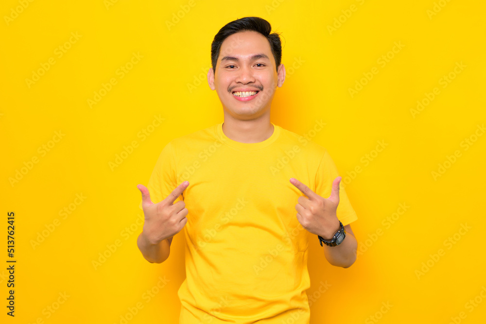 Smiling young Asian man in casual t-shirt pointing fingers at himself with proud isolated on yellow background. People lifestyle concept Smiling young Asian man in casual t-shirt pointing fingers at himself with proud isolated on yellow background. People lifestyle concept
