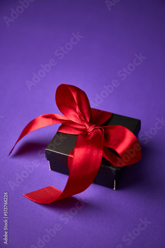 black gift with red ribbon on purple background. Valentine's day. Birthday or Holidays concept. Copy space