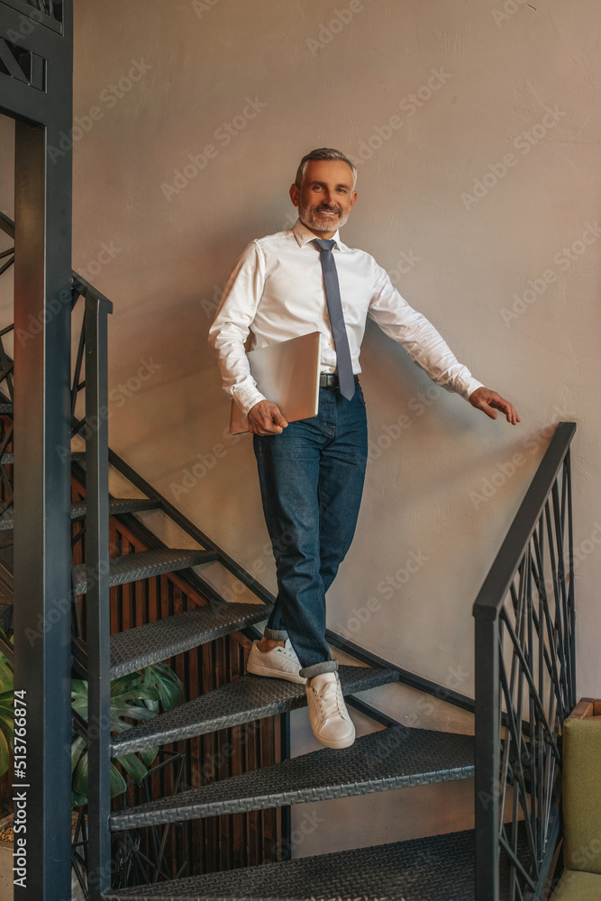 Man with laptop walking down stairs looking at camera