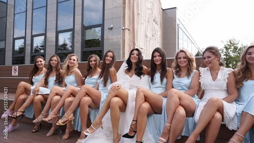 Attractive bride and bridesmaids switching crossing legs sitting on bench seductively in provocative way. Pretty women in identical dresses cross legs simultaneously together flirting at camera. photo