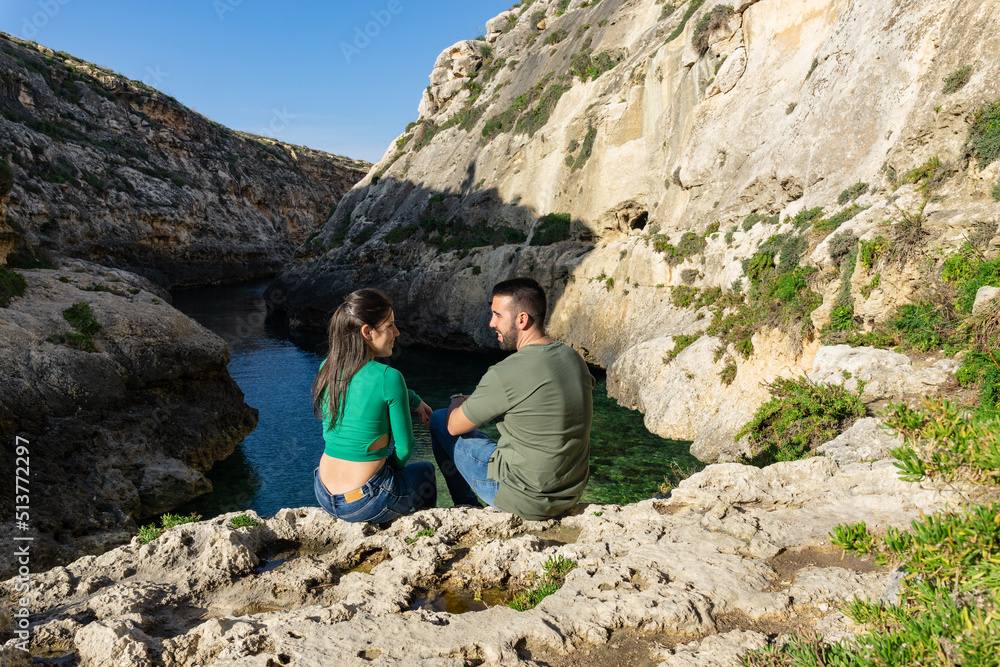 Couple looking at each other while sitting on a rock at Wied Il-Ghasri in Gozo Malta