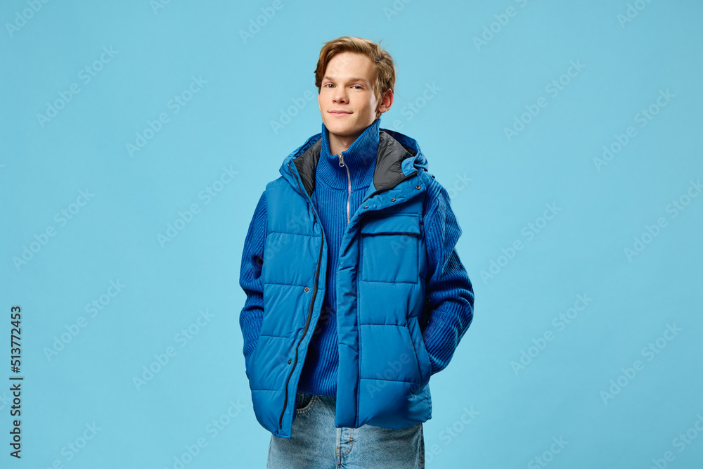 a young man dressed in a fashionable blue warm vest posing on a light blue background with empty space for text a young man dressed in a fashionable blue warm vest posing on a light blue background with empty space for text