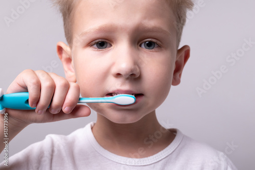 blond boy in a white t-shirt brushing his teeth