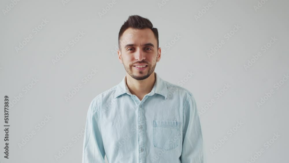 Young Caucasian Brunet Man is Looking at the Camera on a Light Gray Background. Studio Male Face Portrait. Natural Day Light. Young Caucasian Brunet Man is Looking at the Camera on a Light Gray Background. Studio Male Face Portrait. Natural Day Light.