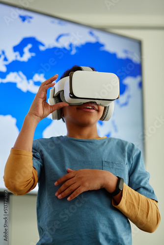 Vertical portrait of young black boy using VR in school classroom with geography map in background