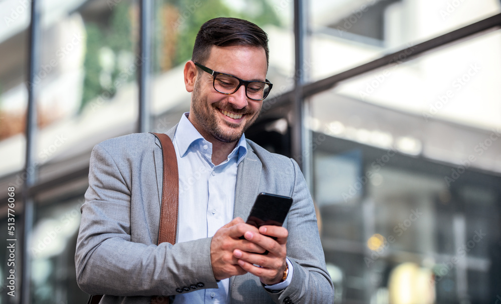 Successful smiling businessman standing in front of the corporation and checking data on smartphone. Business, education, lifestyle concept Successful smiling businessman standing in front of the corporation and checking data on smartphone. Business, education, lifestyle concept