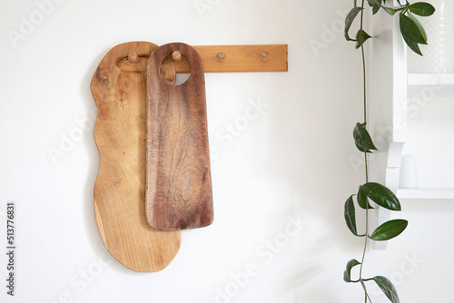 Wooden cutting board collection hang on the wall. Cozy rustic style modern kitchen interior detail, green plant and white shelf. Decoration in traditional kitchen.
