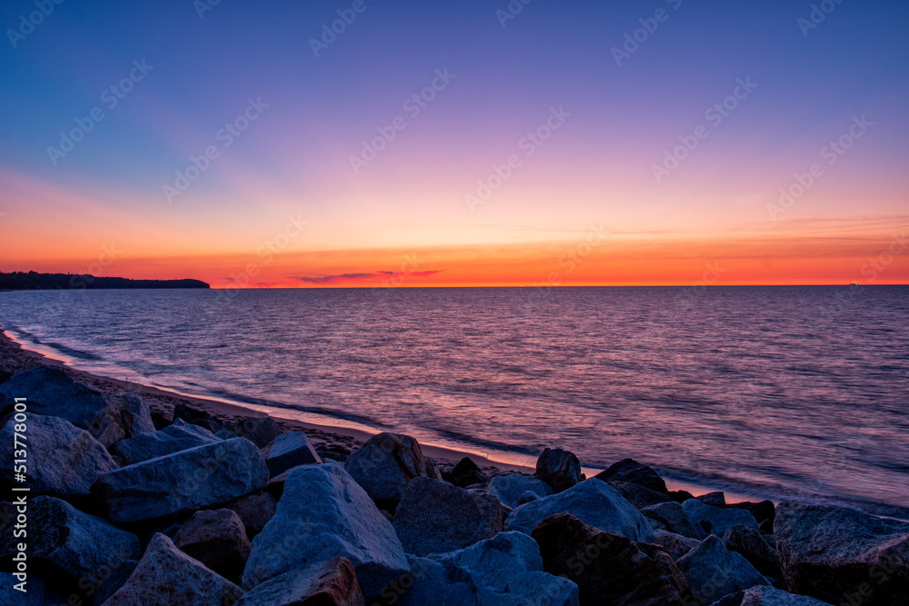Niesamowity zachód słońca nad morzem. Fale uderzające o kamienne głazy na brzegu plaży