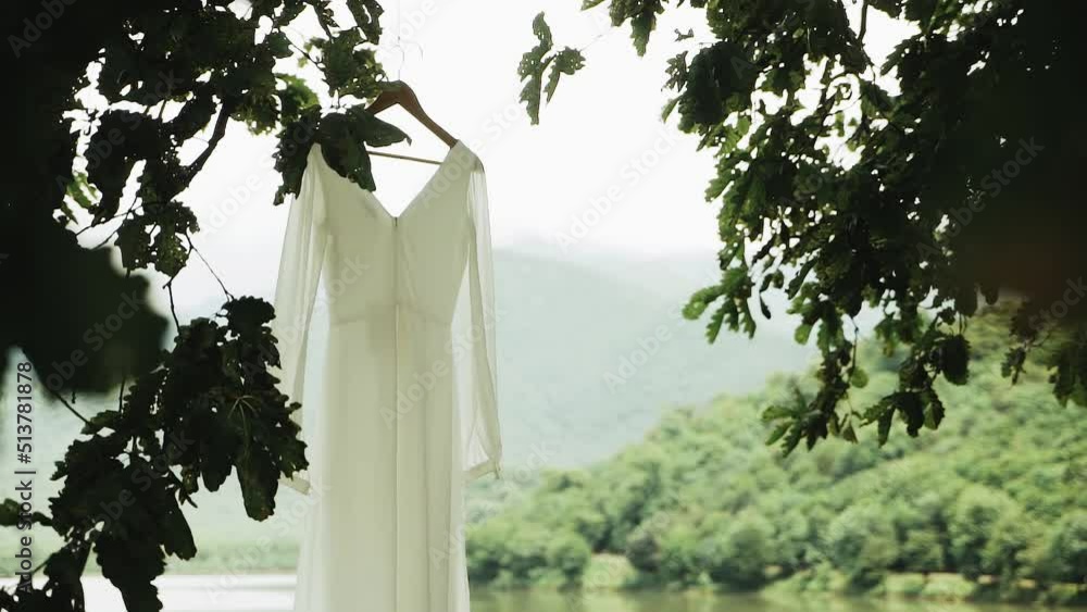 Beautiful designer wedding dress gown swaying in the breeze as it hangs from tree and the lake and mountains on the background. Beautiful designer wedding dress gown swaying in the breeze as it hangs from tree and the lake and mountains on the background.