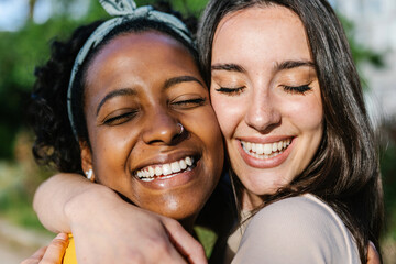 Candid happy multiracial best women friends embracing outdoors - Close up view of two diverse girls hugging each other with closed eyes smiling - Female friendship