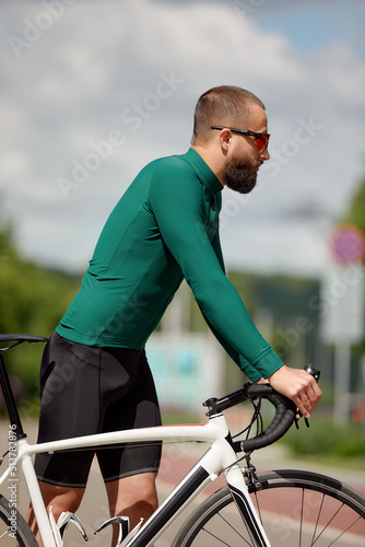 Portrait of a sporty man in a cycling outfit standing with a bicycle on the Bike Lane, posing for the camera