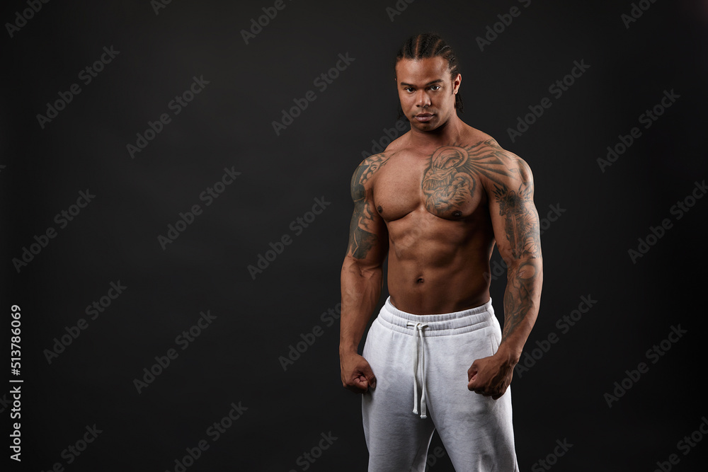 Fototapeta premium Handsome shirtless muscular black young man, looking at camera, on dark background in studio shot