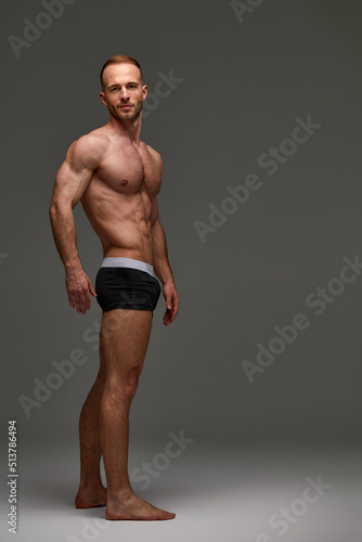 Young male athlete posing. Handsome athletic male power guy. Fitness muscular person. Young athlete showing muscles in the studio, posing shirtless on gray background. © Georgii
