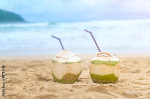 Fresh coconut with drinking straw on the beach, travel and holidays concept.