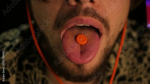 Slow mo cinematographic shot of bearded man eating bright orange disco pill. Close up of man putting ecstasy pill on tongue and swallowing it. Concept of partying long and hard with banned tablets
