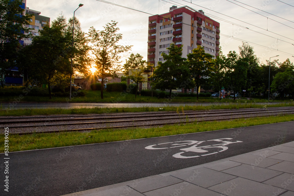 Zachód słońca w mieście. Ścieżka rowerowa, linia tramwajowa, ulica. Blokowisko. - obrazy, fototapety, plakaty 