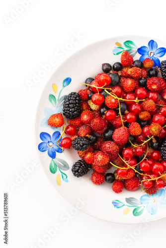 Fresh berries on a plate on a white background, red and black currants and black mulberries, wild strawberries and cherries, top view