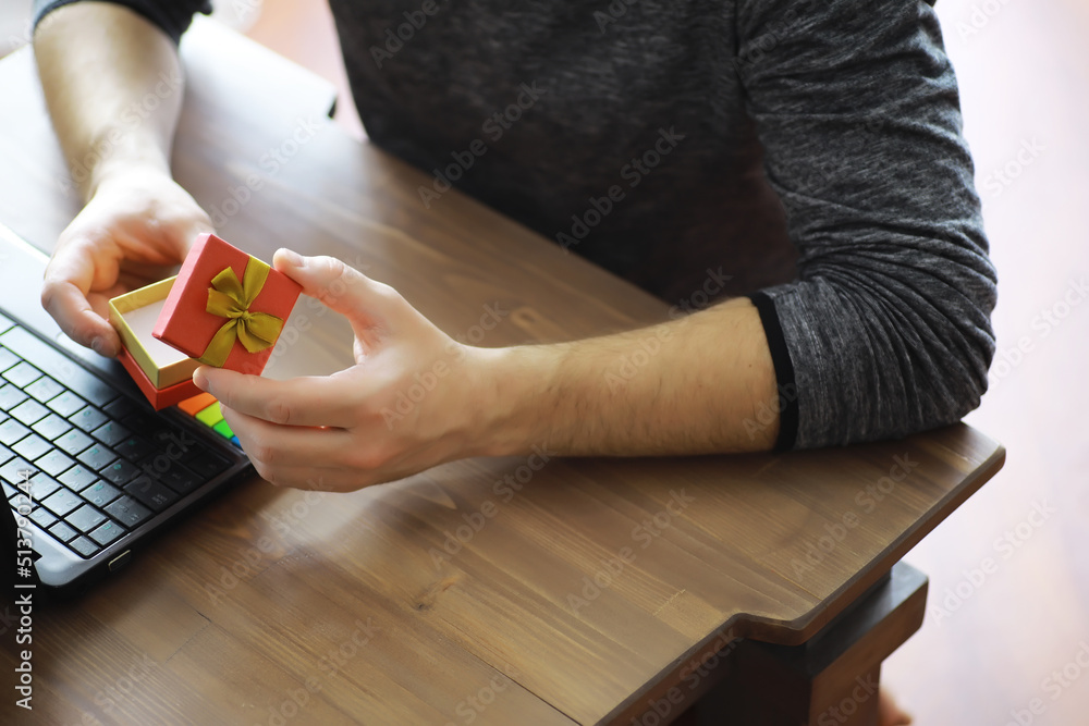 Obraz premium A man with a gift in his hand sits in front of the monitor screen. Order a gift for home and office.
