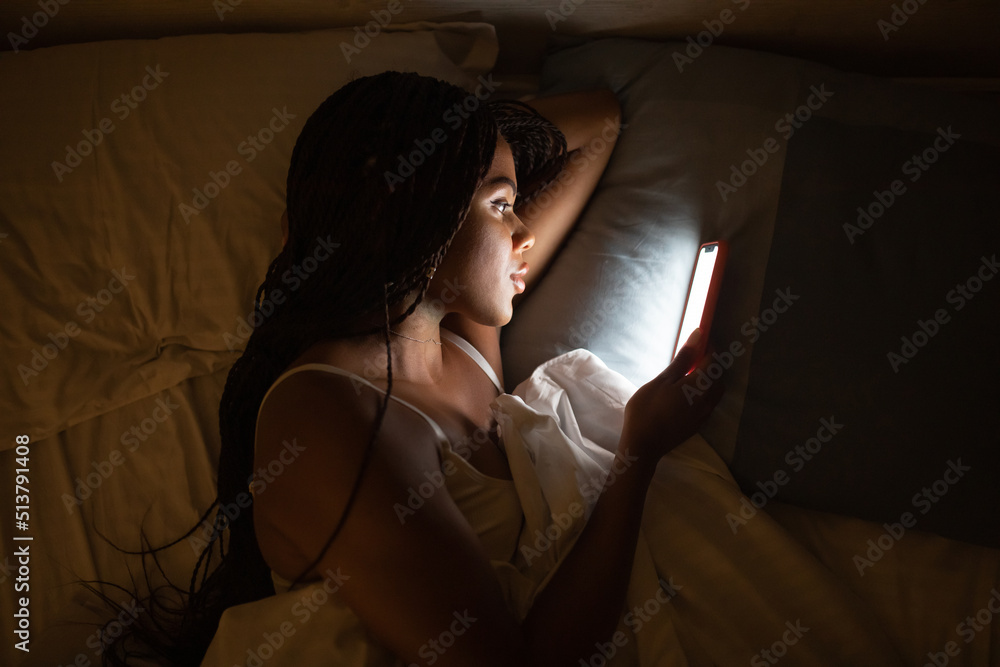 Close up portrait African American woman looking at phone while in bed.