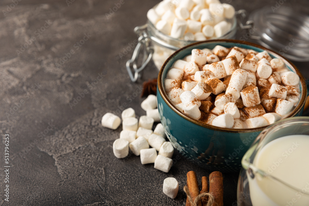 Cup of tasty cocoa drink and marshmallows in blue cup.Spices and marshmallows for winter drinks on black texture table.Winter hot drink.Hot chocolate with marshmallow and spices.Copy space. Cup of tasty cocoa drink and marshmallows in blue cup.Spices and marshmallows for winter drinks on black texture table.Winter hot drink.Hot chocolate with marshmallow and spices.Copy space.