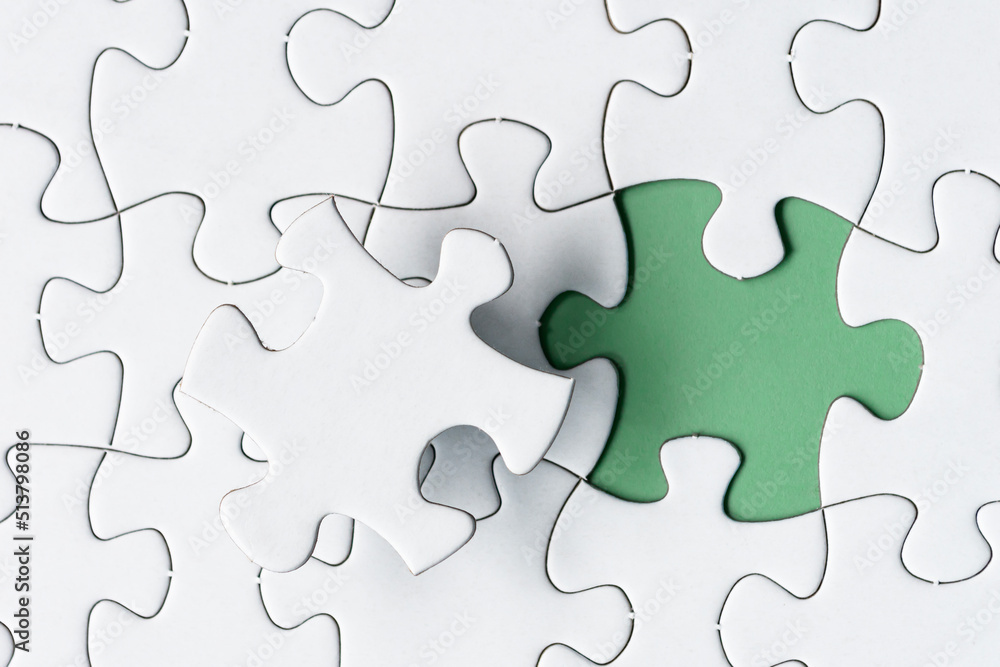 White jigsaw puzzle with missing piece on green background. Copy space. White jigsaw puzzle with missing piece on green background. Copy space.