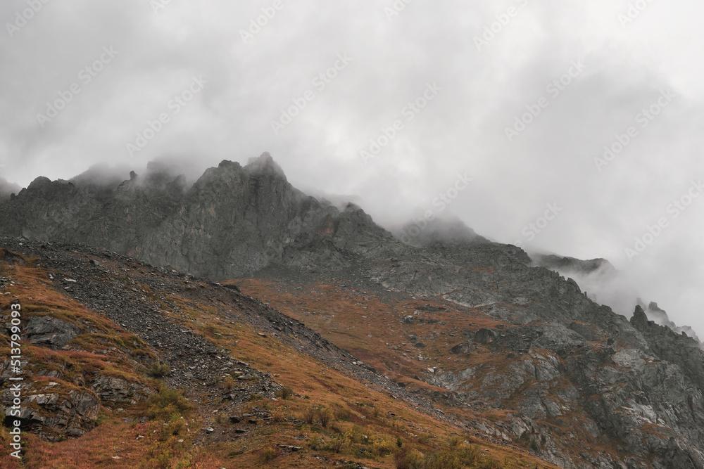 Mystical background with dramatic mountains. Rain in mountains. Atmospheric misty landscape with fuzzy silhouettes of sharp rocks in low clouds during rain.