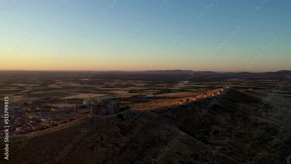 Aerial view of Windmill of Consuegra. Underexposed video at sunrise. View of the castle of Consuegra. Beautiful Warm colours. Drone dolly backward. Noise in shadows Aerial view of Windmill of Consuegra. Underexposed video at sunrise. View of the castle of Consuegra. Beautiful Warm colours. Drone dolly backward. Noise in shadows