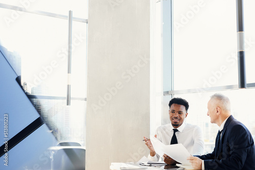 Cheerful successful business colleagues in formal outfits sitting at table in modern office and examining documents together photo