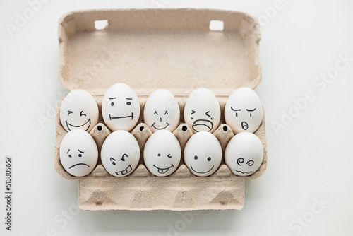 Eggs with funny faces in carton package on white wooden table