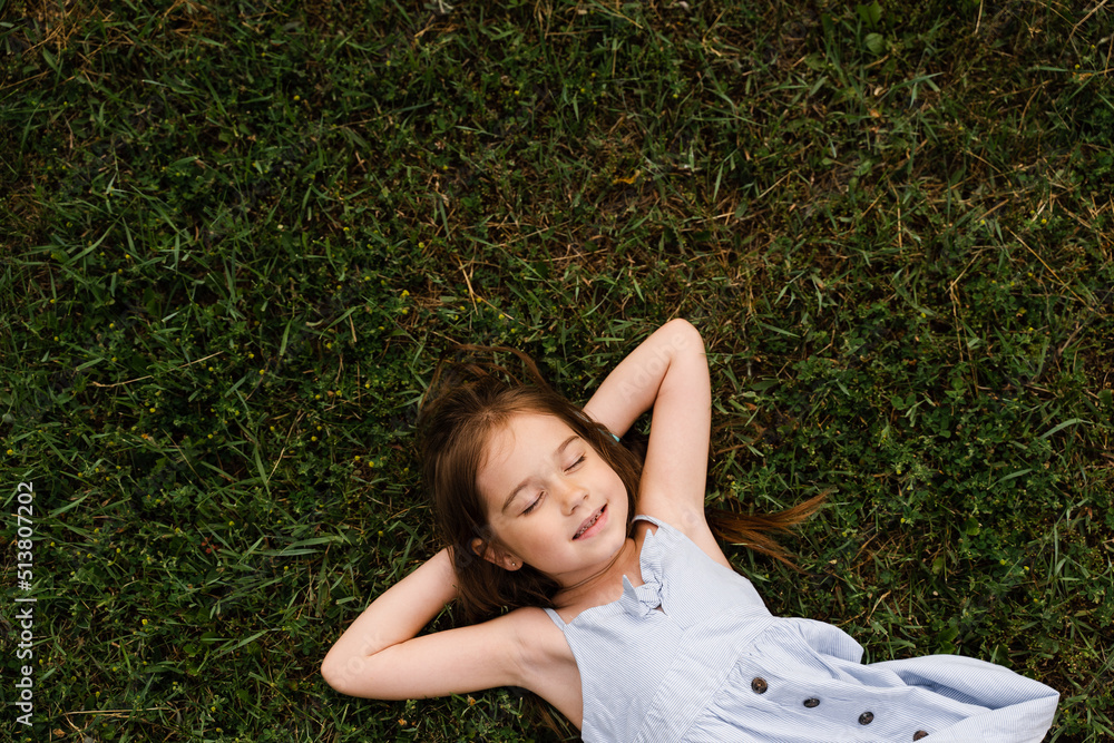 Calm child girl lay on the grass with closed eyes and enjoy life. Lifestyle of happy toddler. Kid relaxing on the grass. Calm child girl lay on the grass with closed eyes and enjoy life. Lifestyle of happy toddler. Kid relaxing on the grass.