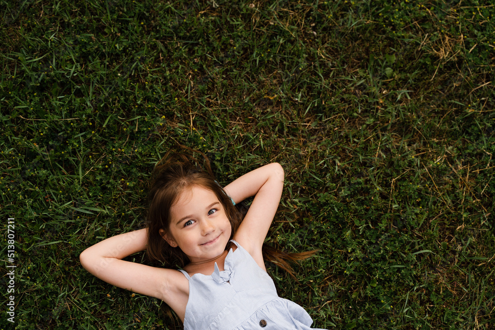 Happy child girl lay on the grass, enjoy life and smile. Lifestyle of happy toddler. Kid relaxing on the grass. Happy child girl lay on the grass, enjoy life and smile. Lifestyle of happy toddler. Kid relaxing on the grass.