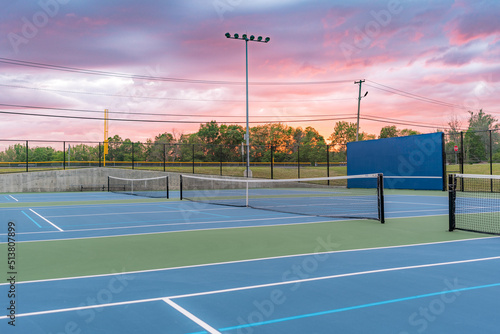 Evening photo of outdoor blue tennis courts with pickleball lines with lights turned on.  © Thomas