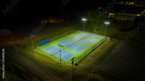 Evening aerial photo of outdoor blue tennis courts with pickleball lines with lights turned on. 