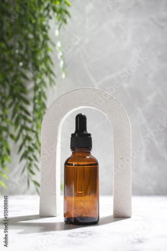 Cosmetic bottle serum or oil in arch on grey marble background. Natural cosmetics concept, skin care product. Beauty concept for face body care