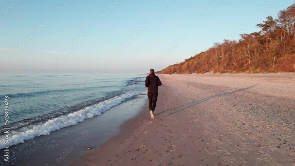A runner, at sunset, he runs along the beach along the waves. A runner, at sunset, he runs along the beach along the waves.