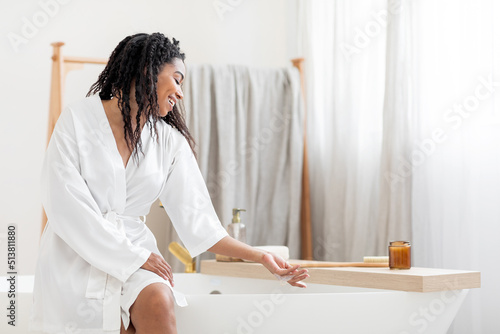 Home Spa. Beautiful Black Woman Sitting On Bathtub And Touching Foam