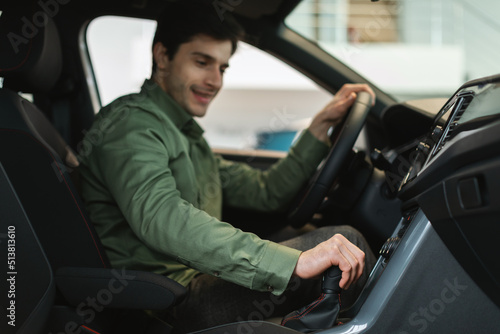 Cheerful young Caucasian guy test driving new car before purchase at automobile dealership, selective focus