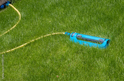blue color lawn sprinkler on green grass texture.summer sunny day.lawn watering concept in drought days,garden irrigation.sprinkler lying,hidden in grass.